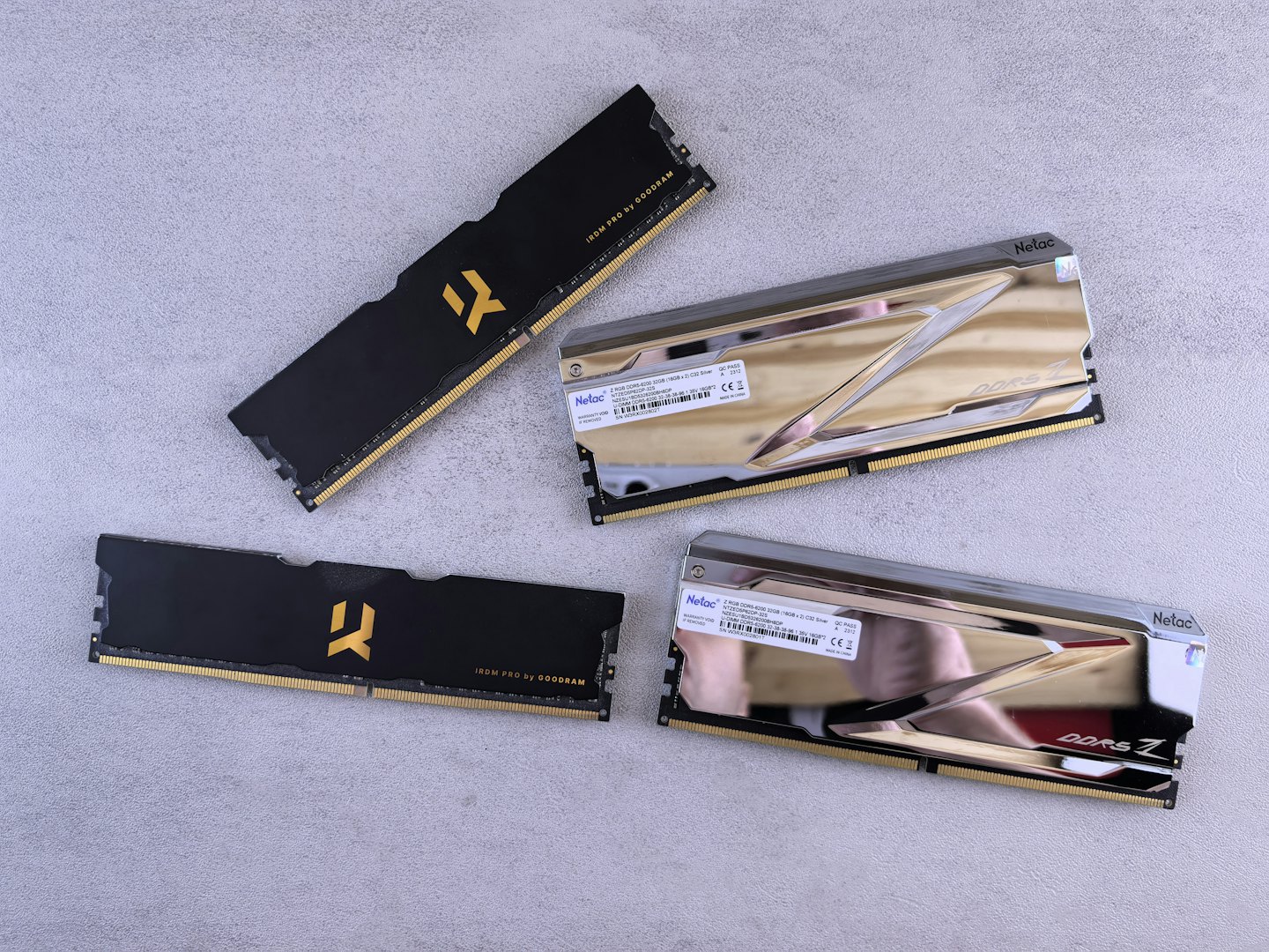 Quattro moduli RAM per computer disposti diagonalmente su una superficie grigia.